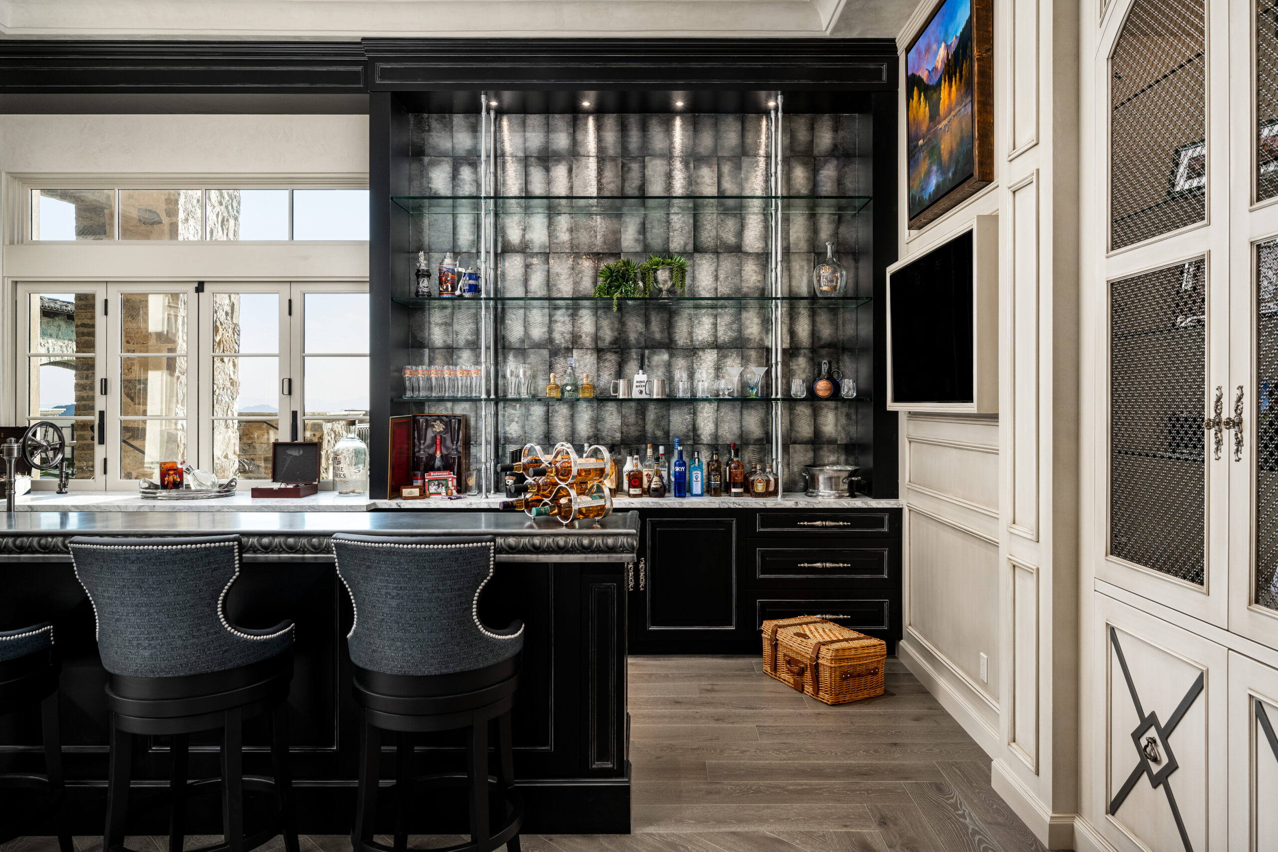 Close-Up of Home Bar Shelving and Counter: A close-up view of the home bar, highlighting the glass shelves displaying various bottles, a dark countertop, and bar stools. The backdrop is a textured grey wall with modern lighting, and there are cabinets with glass doors for additional storage.